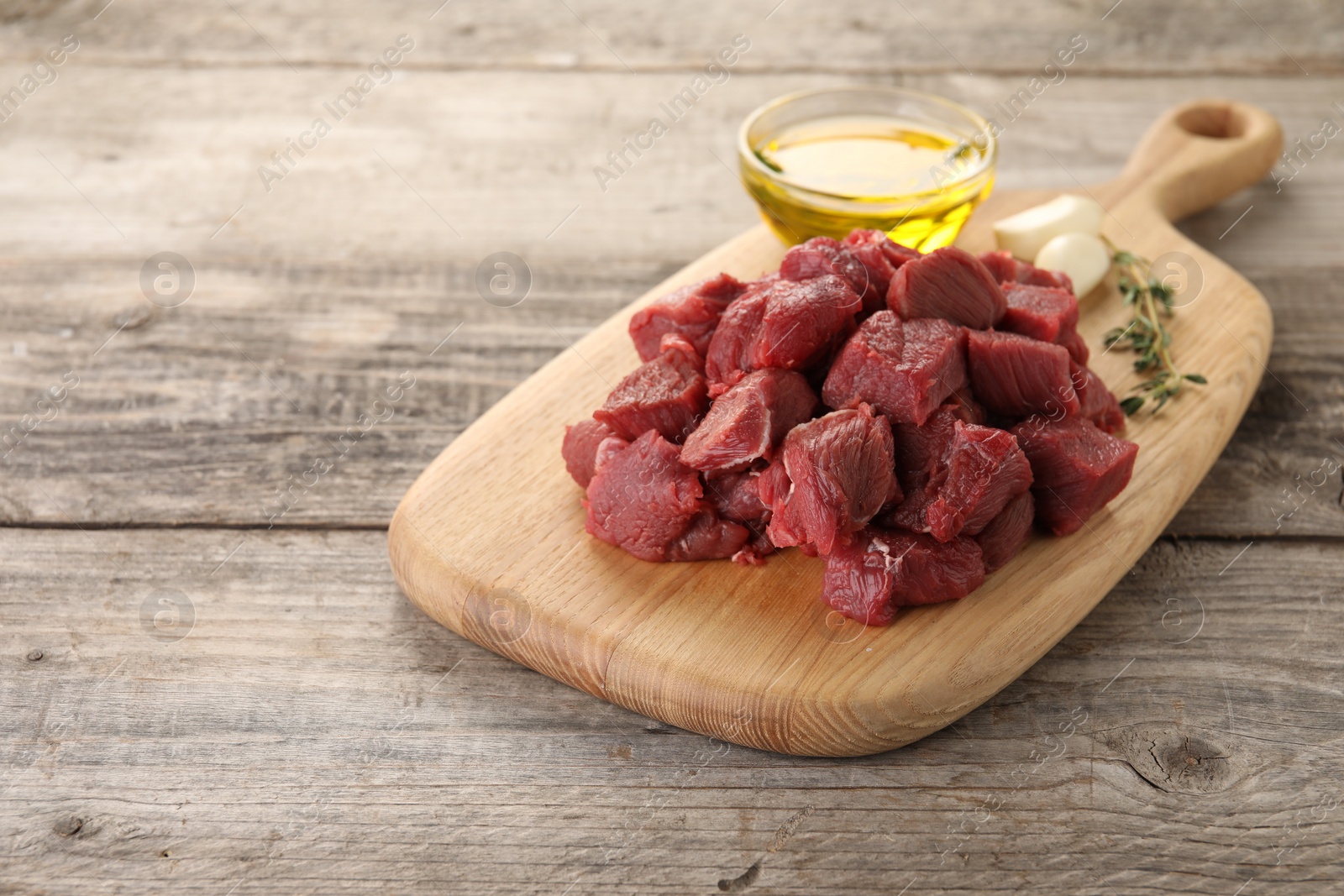 Photo of Pieces of raw beef meat, oil and garlic on wooden table