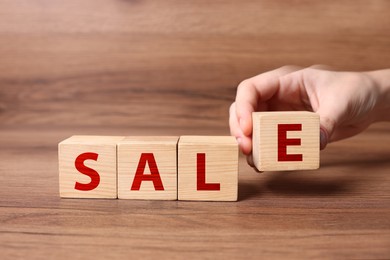 Image of Woman making word Sale with cubes on wooden table, closeup