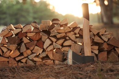 Stack of cut firewood and axe in forest, closeup