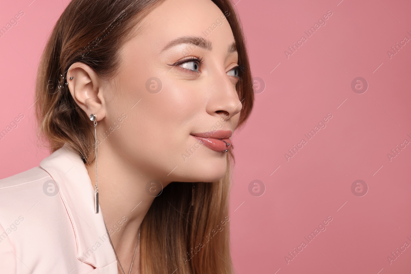 Photo of Young woman with lip and ear piercings on pink background, space for text