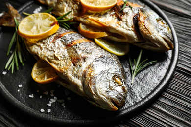 Photo of Delicious roasted fish with lemon on black wooden table, closeup