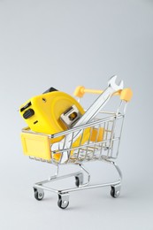 Photo of Metal wrench and measuring tape in shopping cart on light grey background