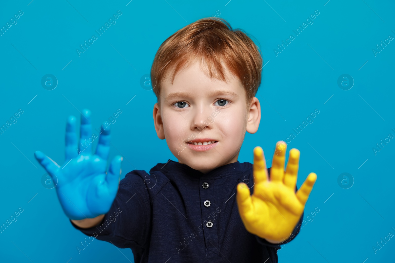 Photo of Little boy with hands painted in Ukrainian flag colors on light blue background. Love Ukraine concept