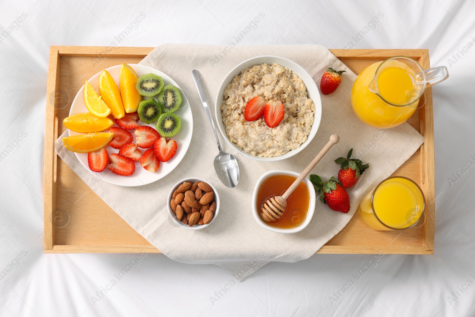 Tasty breakfast served in bed. Oatmeal, juice, fruits, almonds and honey on tray, top view Photo of Tasty breakfast served in bed. Oatmeal, juice, fruits, almonds and honey on tray, top view