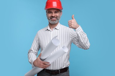 Photo of Architect in hard hat holding drafts and showing thumb up on light blue background