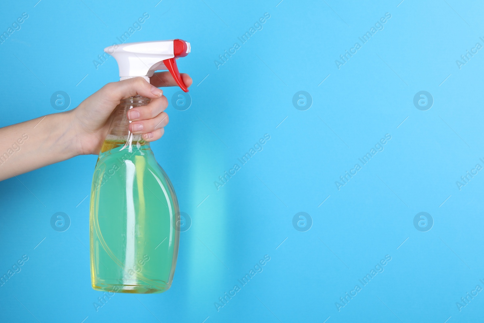 Photo of Woman holding plastic spray bottle on light blue background, closeup. Space for text