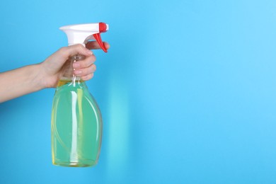 Photo of Woman holding plastic spray bottle on light blue background, closeup. Space for text