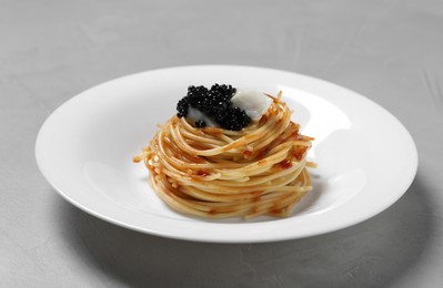 Photo of Tasty spaghetti with tomato sauce and black caviar on light grey table, closeup. Exquisite presentation of pasta dish