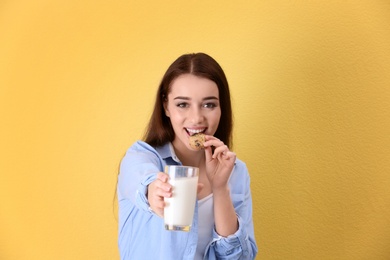 Photo of Beautiful young woman drinking milk with cookie on color background