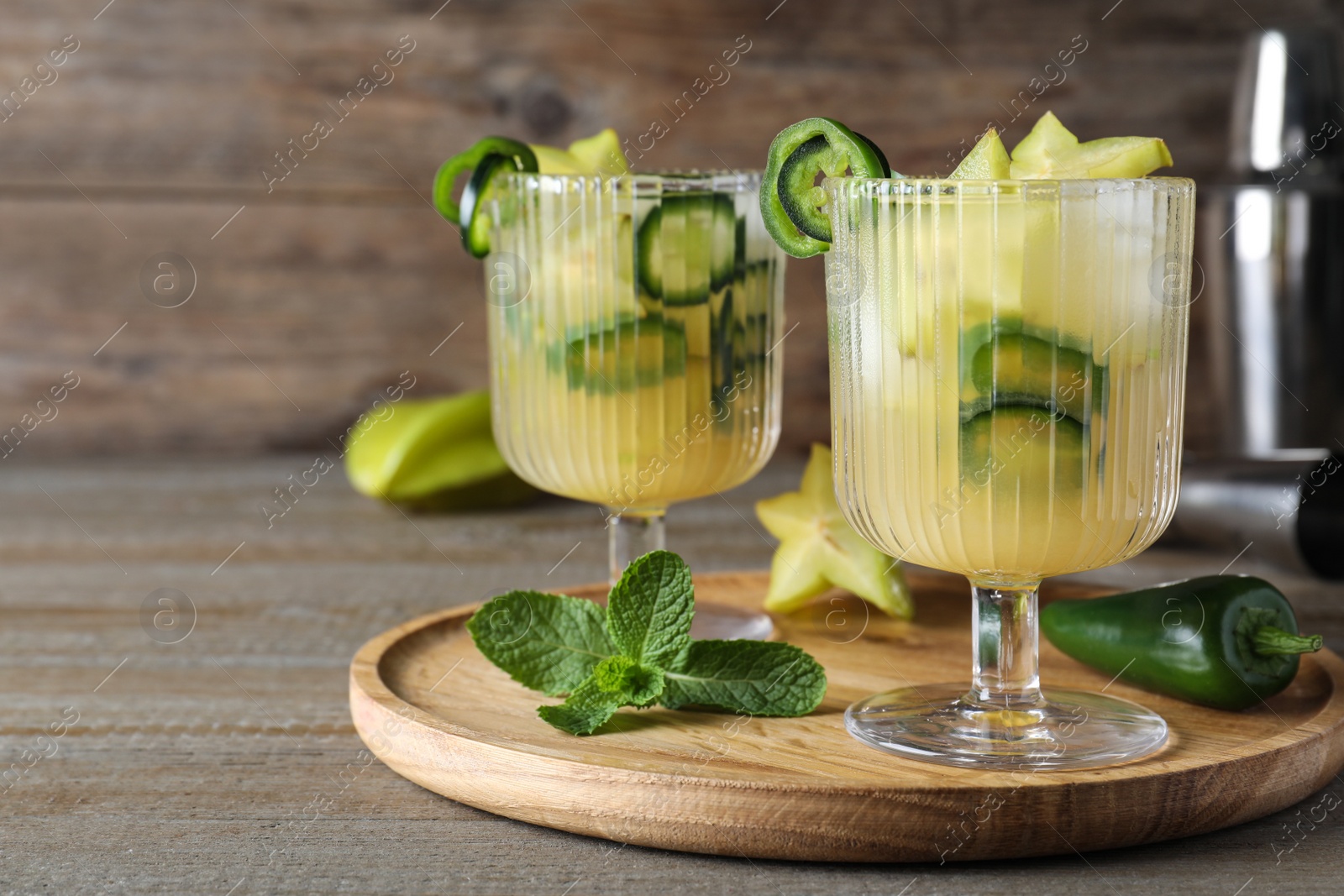 Photo of Glasses of spicy cocktail with jalapeno and carambola on wooden table. Space for text