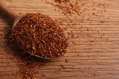 Spoon with dry rooibos leaves on wooden table, above view. Space for text