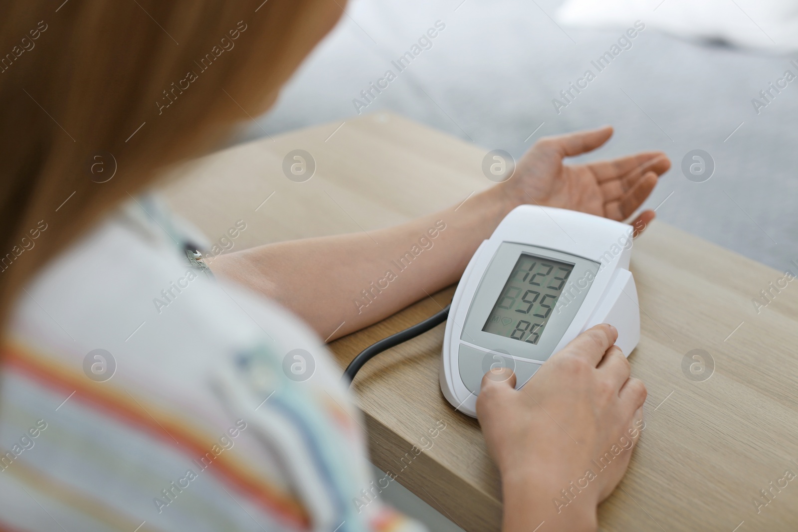 Photo of Woman checking blood pressure with sphygmomanometer at table indoors, closeup. Cardiology concept