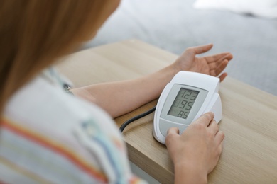 Woman checking blood pressure with sphygmomanometer at table indoors, closeup. Cardiology concept