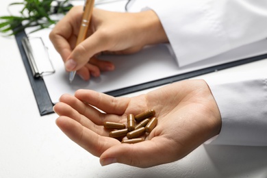 Photo of Female doctor with hemp capsules and clipboard at table, closeup