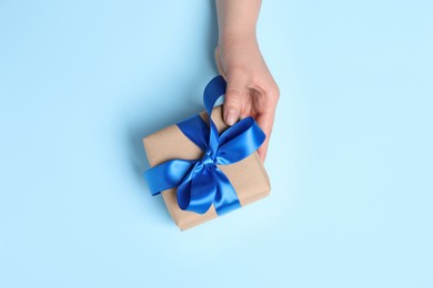 Photo of Woman holding gift box on light blue background, top view