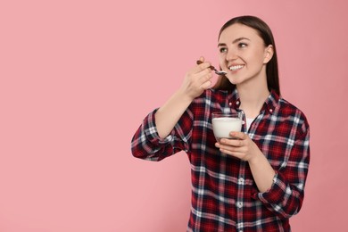 Photo of Woman eating tasty yogurt on pink background, space for text