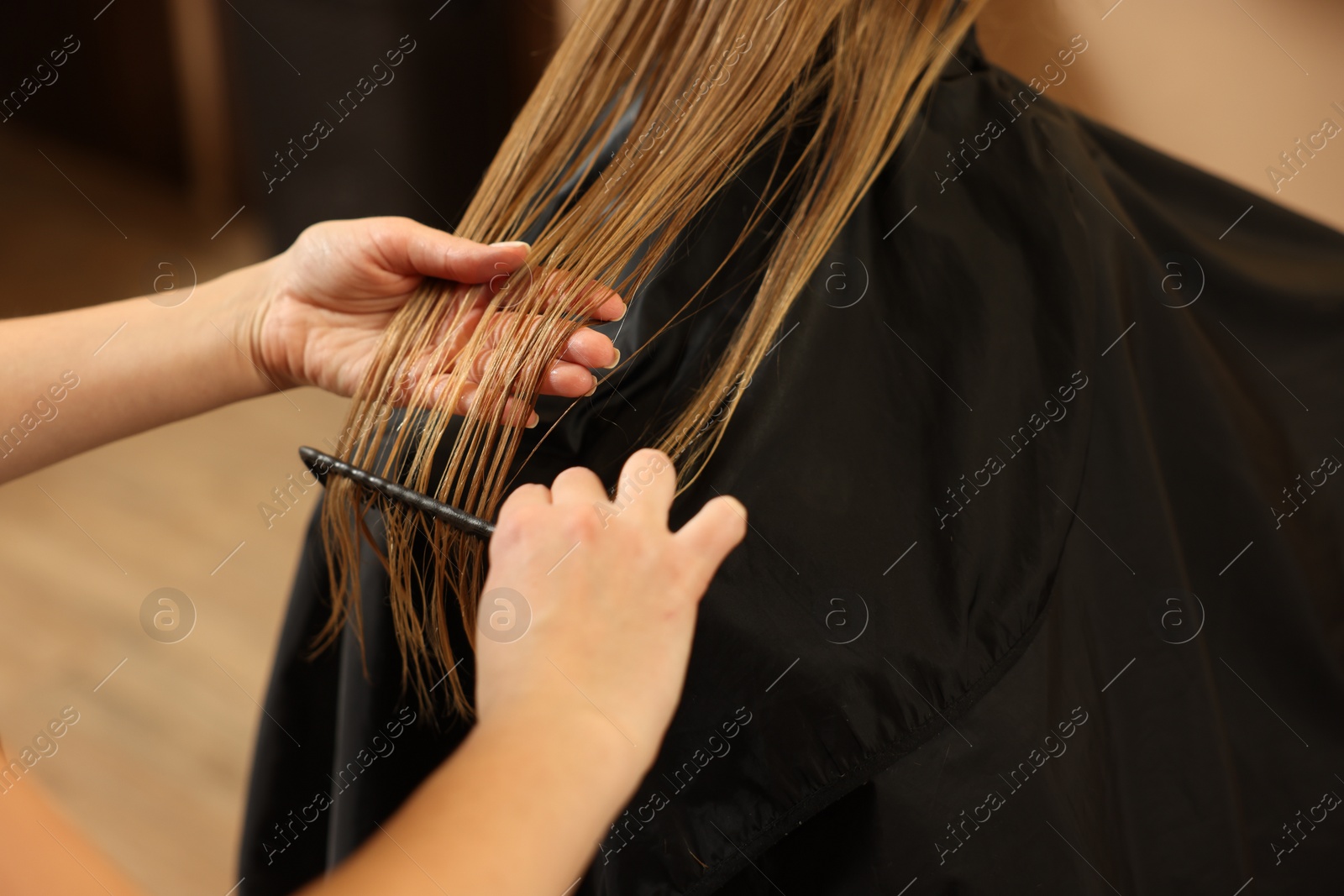 Photo of Professional hairdresser combing girl's hair in beauty salon, closeup