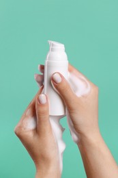 Photo of Woman with foam on hands holding bottle of skin cleanser against green background, closeup. Cosmetic product