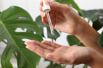 Photo of Woman applying cosmetic serum onto her hand near green plant on white background, closeup