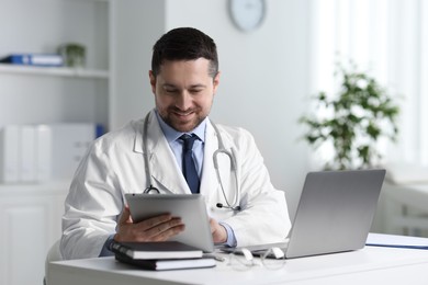 Photo of Smiling doctor having online consultation via tablet at table in clinic