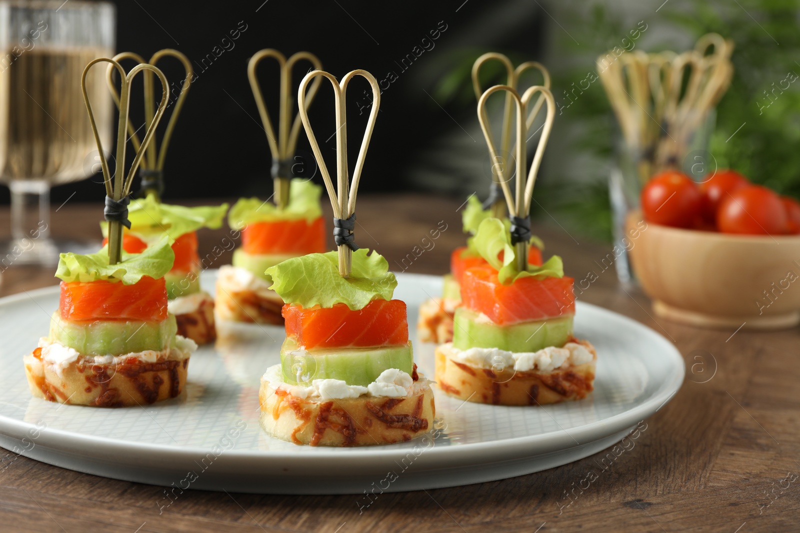 Photo of Tasty canapes with salmon, cucumber, bread and cream cheese on wooden table, closeup