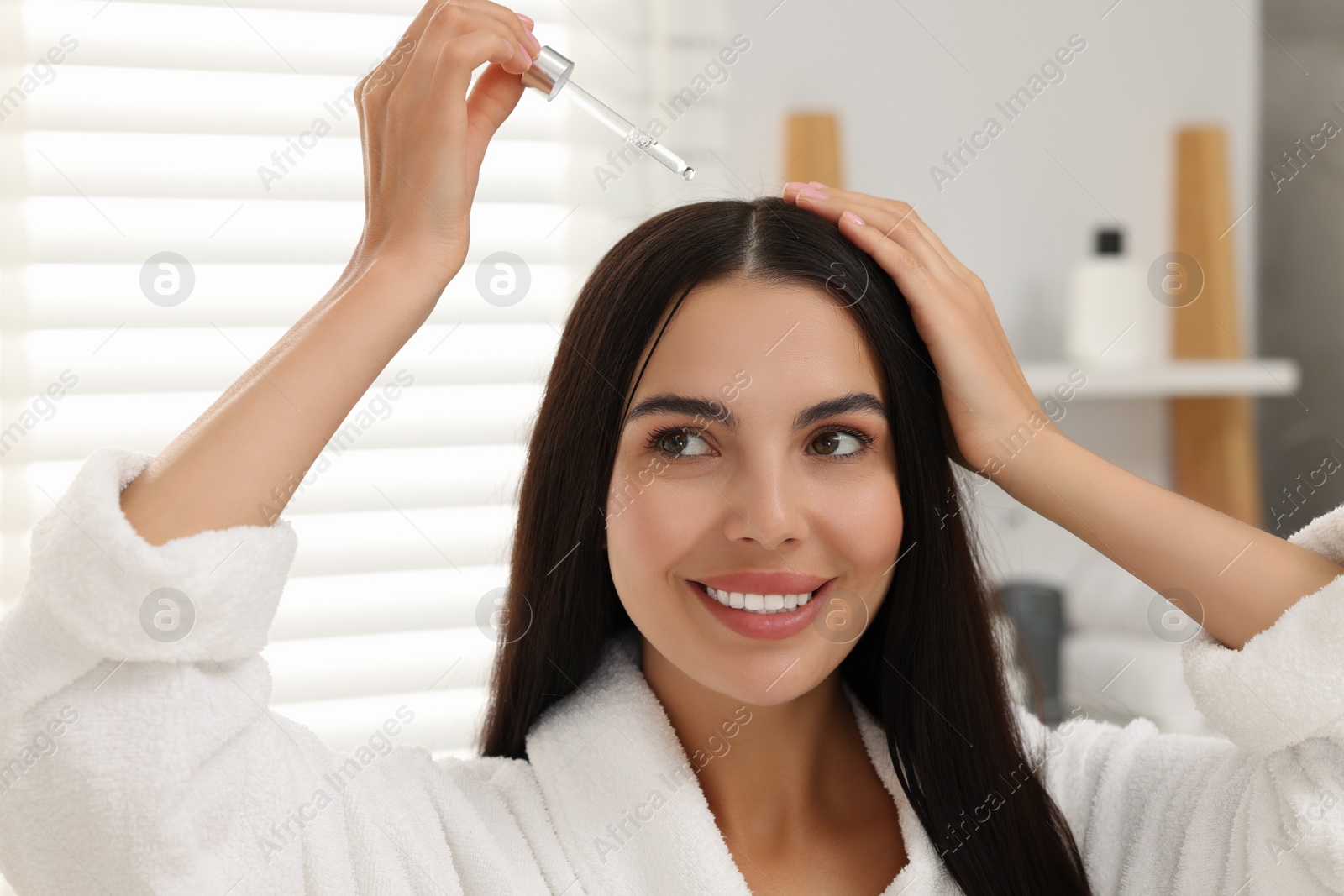 Photo of Beautiful woman applying hair serum in bathroom. Cosmetic product