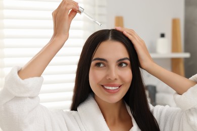 Photo of Beautiful woman applying hair serum in bathroom. Cosmetic product