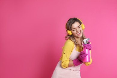 Photo of Beautiful young woman with headphones and bottle of detergent singing on pink background. Space for text