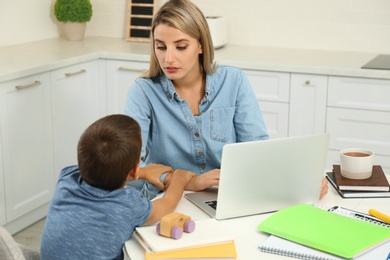 Little boy bothering mother at work in kitchen. Home office concept