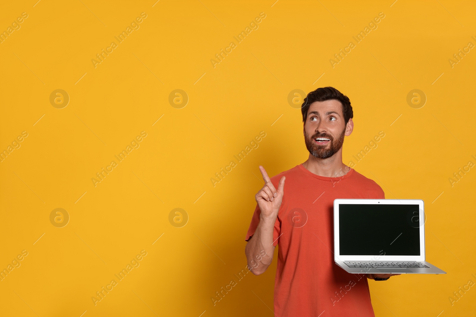 Photo of Handsome man with laptop on orange background