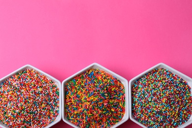 Photo of Colorful sprinkles in bowls on pink background, flat lay with space for text. Confectionery decor