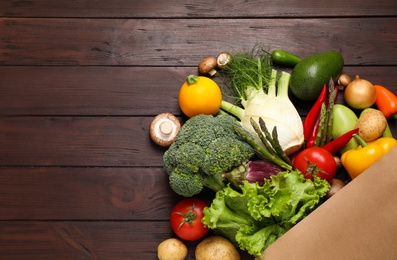 Fresh vegetables in paper shopping bag on wooden table, flat lay. Space for text
