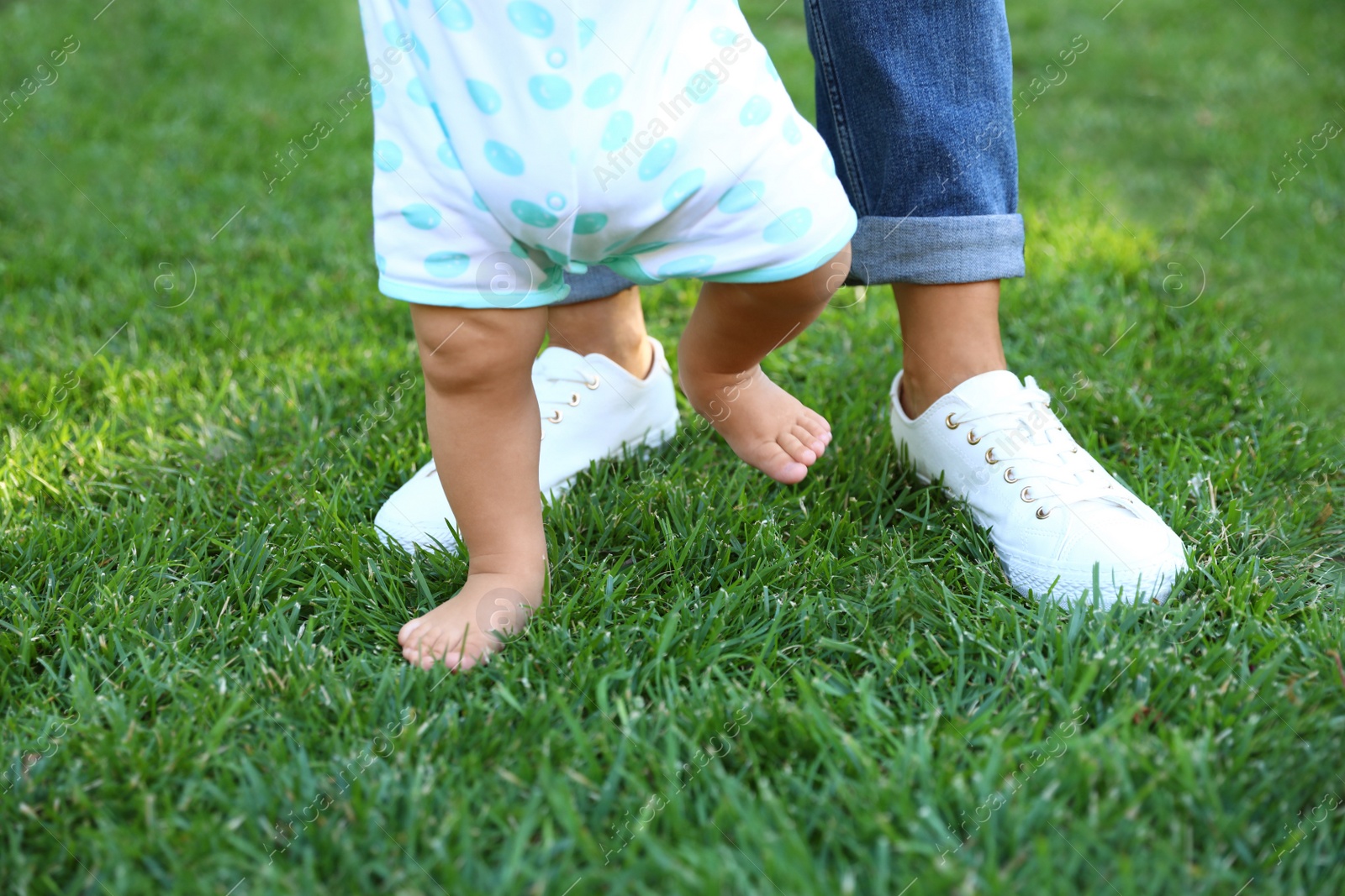 Photo of Cute little baby learning to walk with his nanny on green grass outdoors, closeup