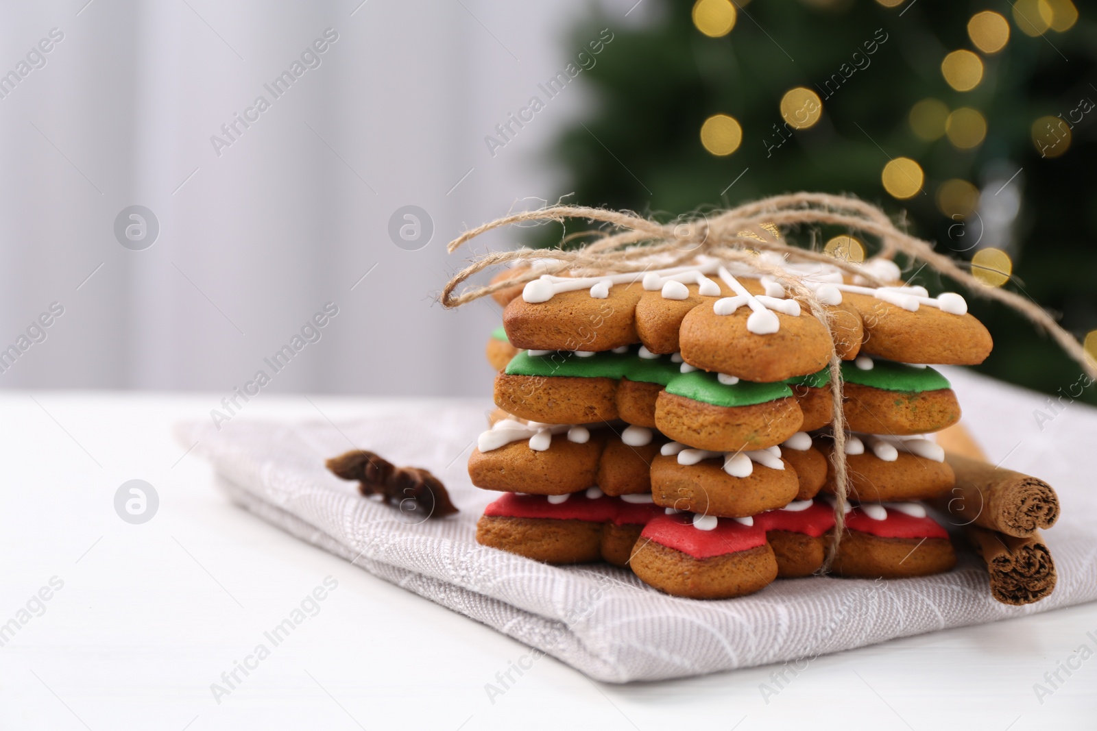 Photo of Decorated cookies on white table against blurred Christmas lights, closeup. Space for text