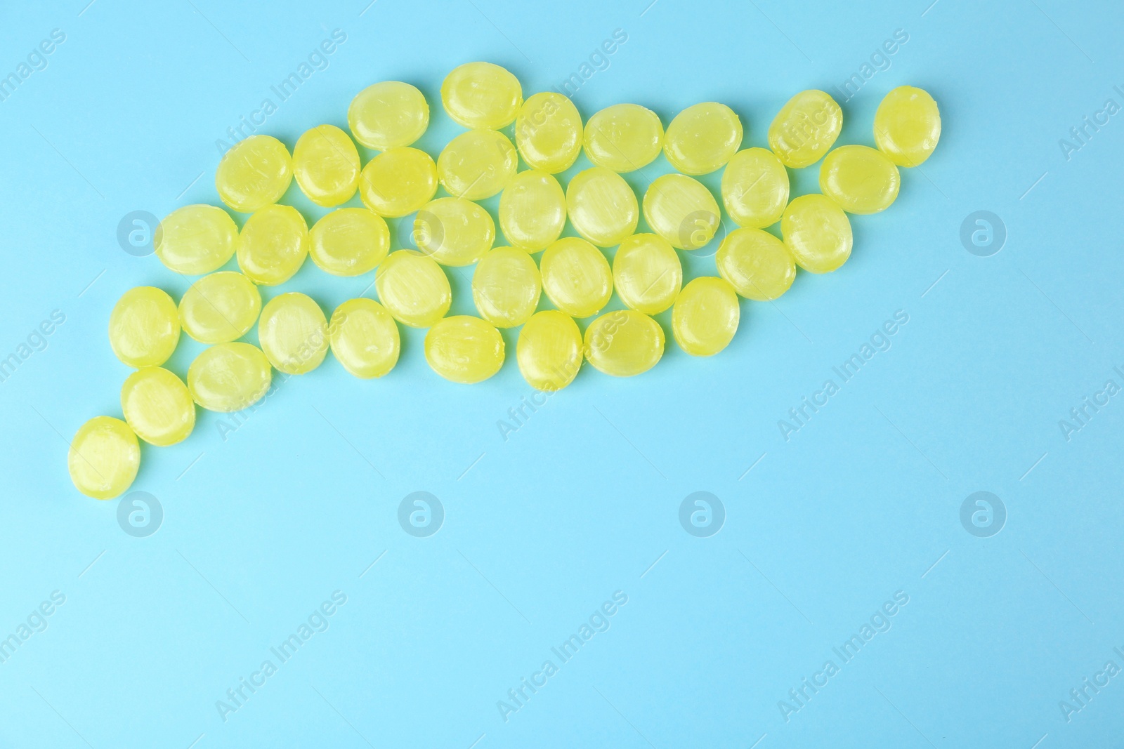 Photo of Delicious lemon drops on light blue background, flat lay. Space for text