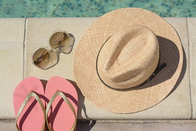 Photo of Stylish hat, flip flops and sunglasses near outdoor swimming pool on sunny day, flat lay. Beach accessories