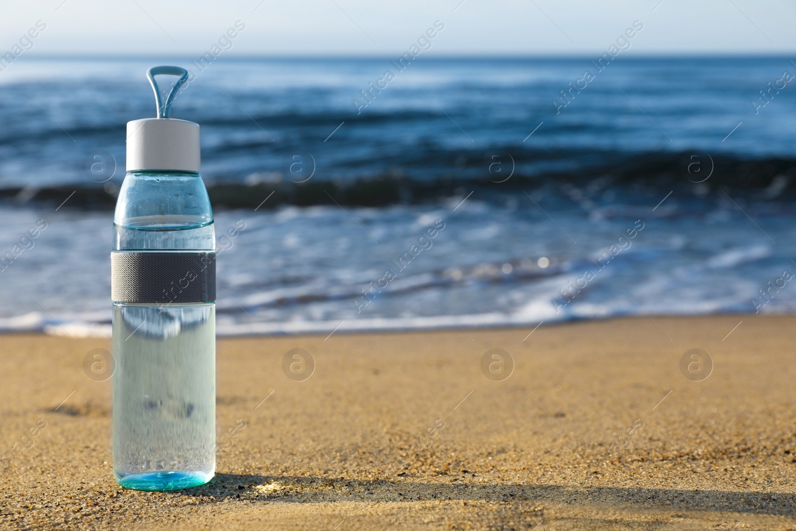 Photo of Glass bottle with water on wet sand near sea. Space for text