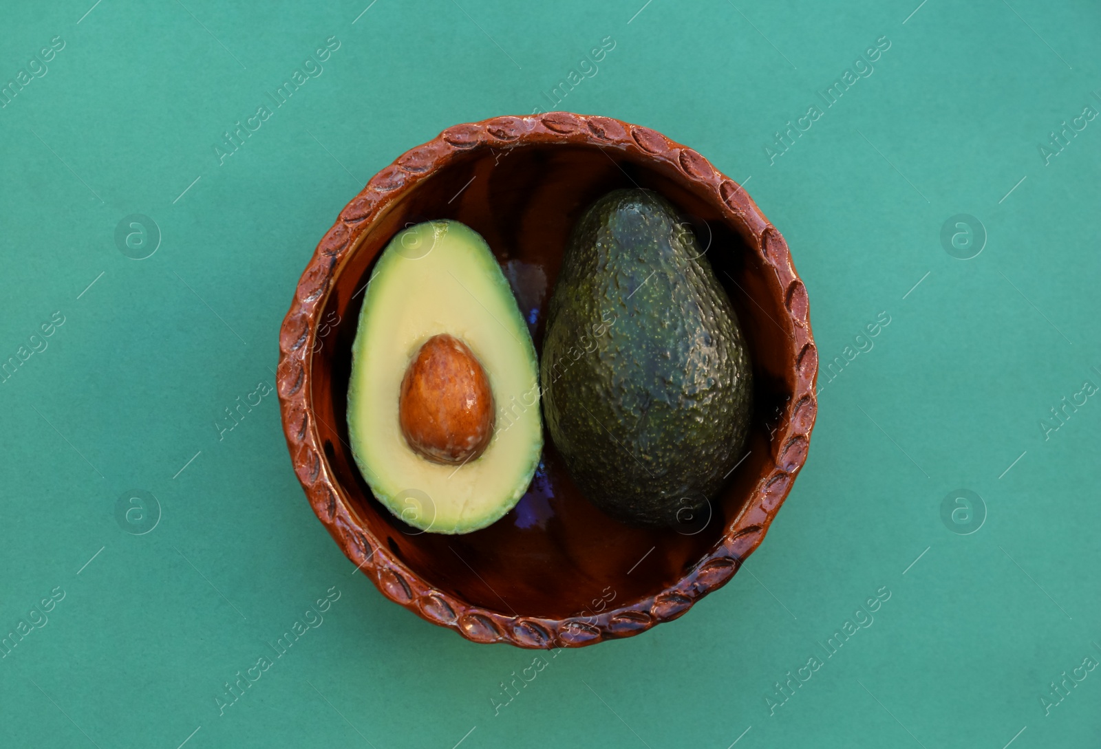 Photo of Tasty fresh avocados in bowl on dark turquoise background, top view