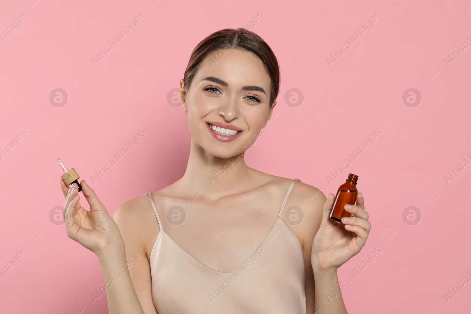 Photo of Young woman with bottle of essential oil on pink background