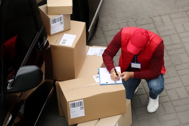 Courier with clipboard and parcels near delivery van outdoors, above view
