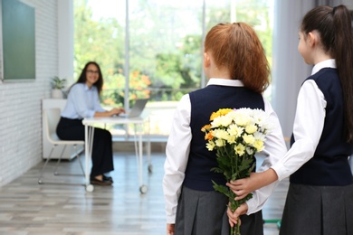 Photo of Schoolgirls with bouquet congratulating their pedagogue in classroom. Teacher's day