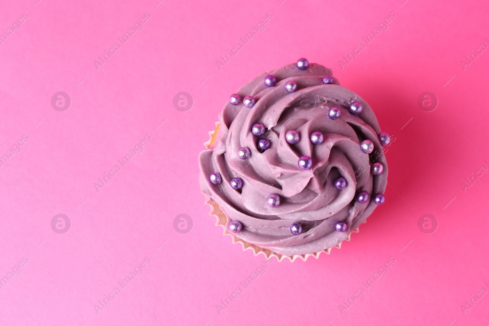 Photo of Delicious cupcake with bright cream and sprinkles on pink background, top view. Space for text