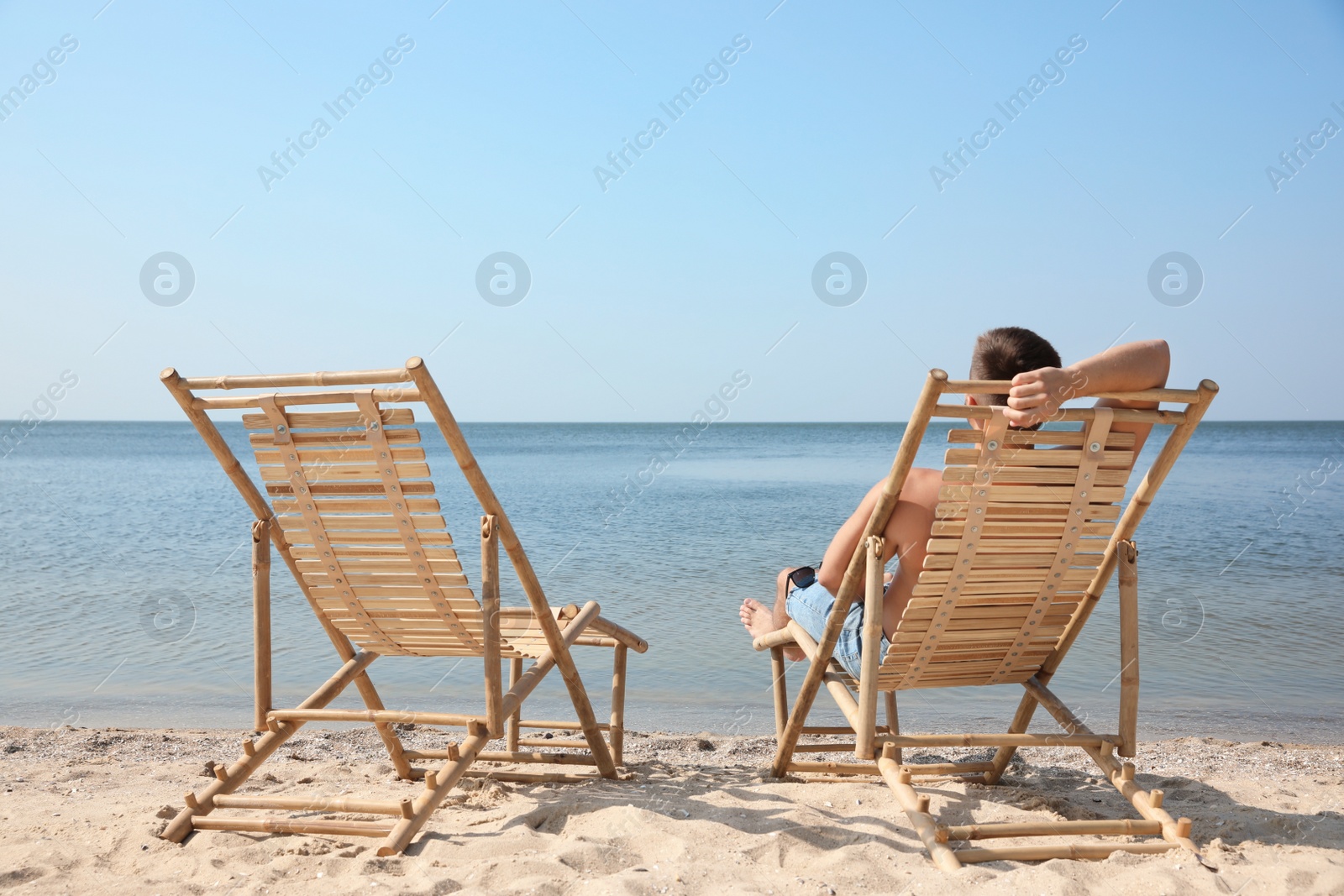 Photo of Young man relaxing in deck chair on sandy beach