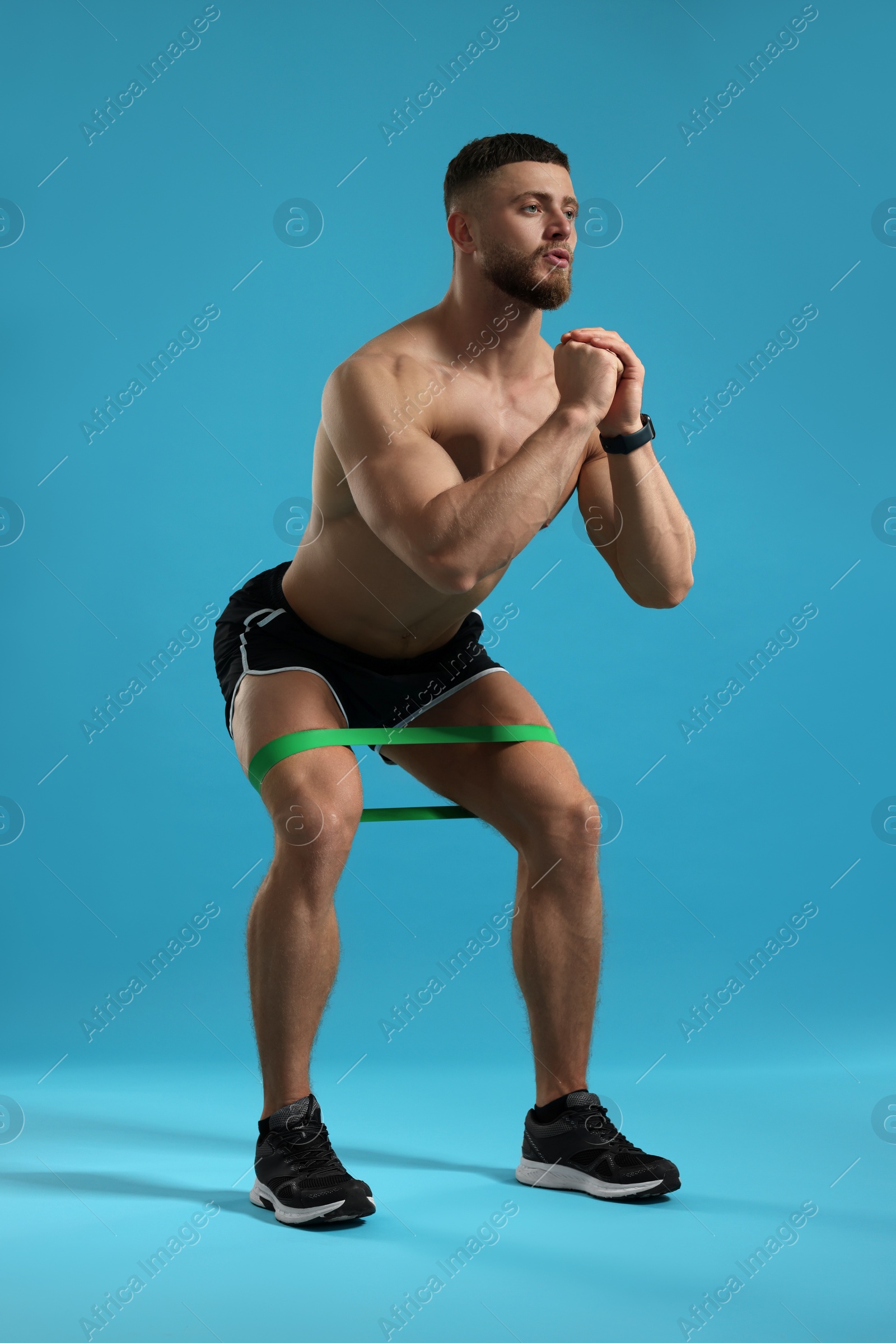 Photo of Muscular man exercising with elastic resistance band on light blue background