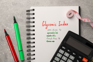 Glycemic Index. Notebook with information, markers, calculator and measuring tape on light grey table, flat lay