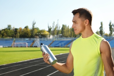 Photo of Sporty man with bottle of water at stadium on sunny day. Space for text