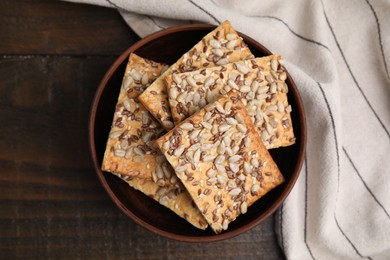 Photo of Cereal crackers with flax, sunflower and sesame seeds in bowl on wooden table, top view