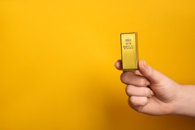 Photo of Woman holding gold bar on orange background, closeup. Space for text