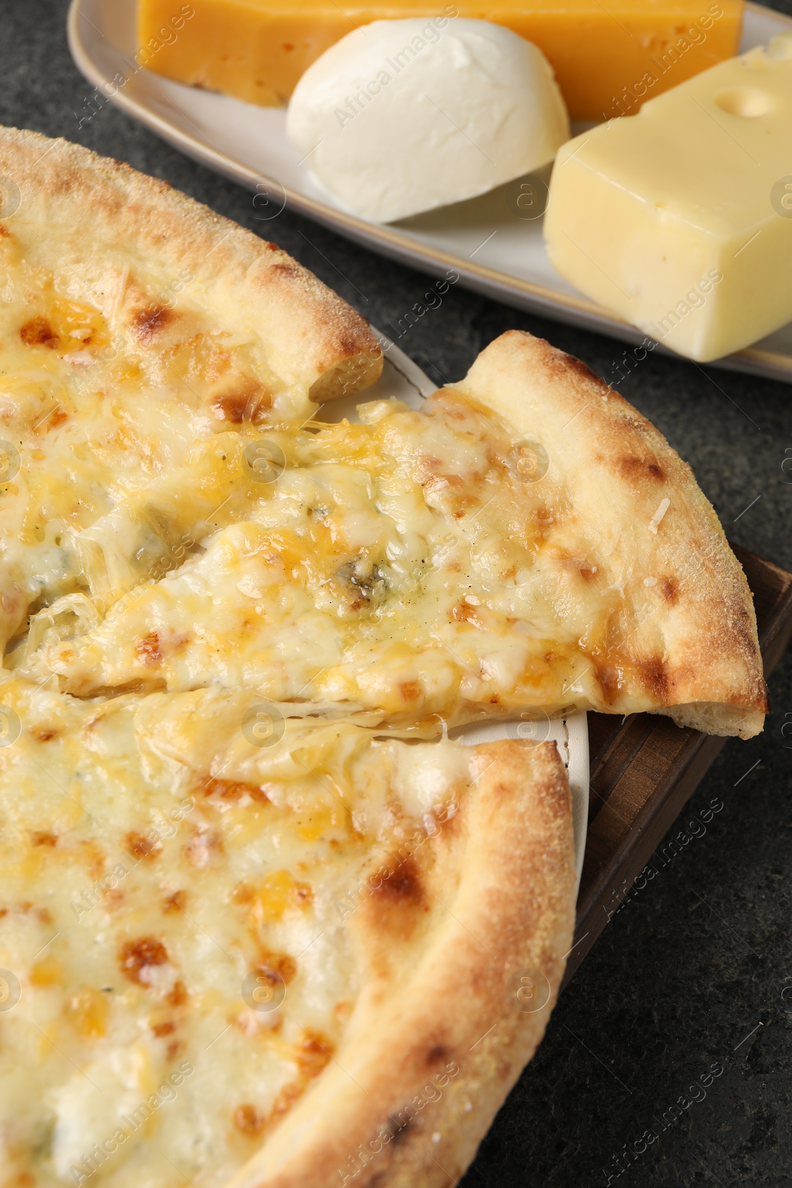 Photo of Delicious cheese pizza and different kinds of cheese on dark grey table, closeup