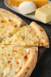 Photo of Delicious cheese pizza and different kinds of cheese on dark grey table, closeup